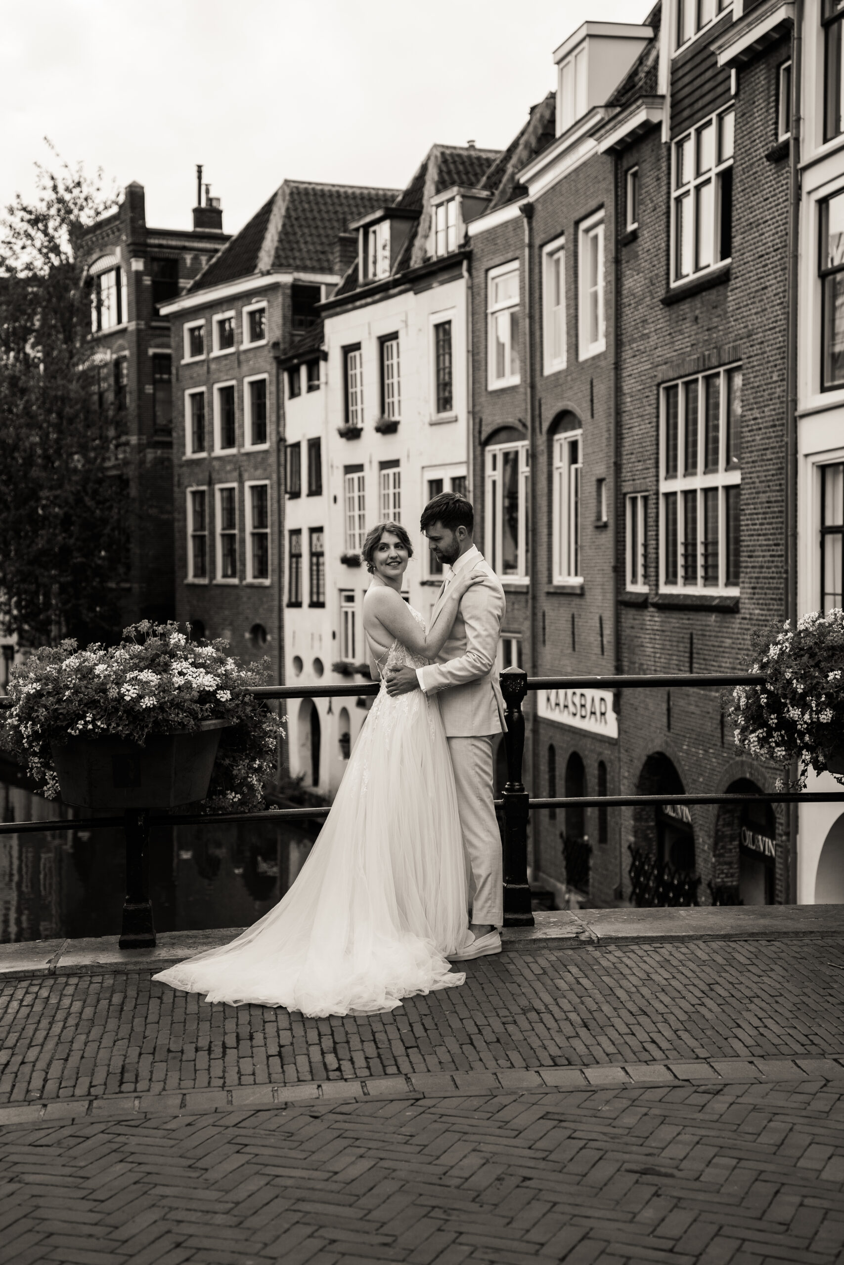 Bruidspaar staat op een Utrechtse gracht en kijkt lachend weg